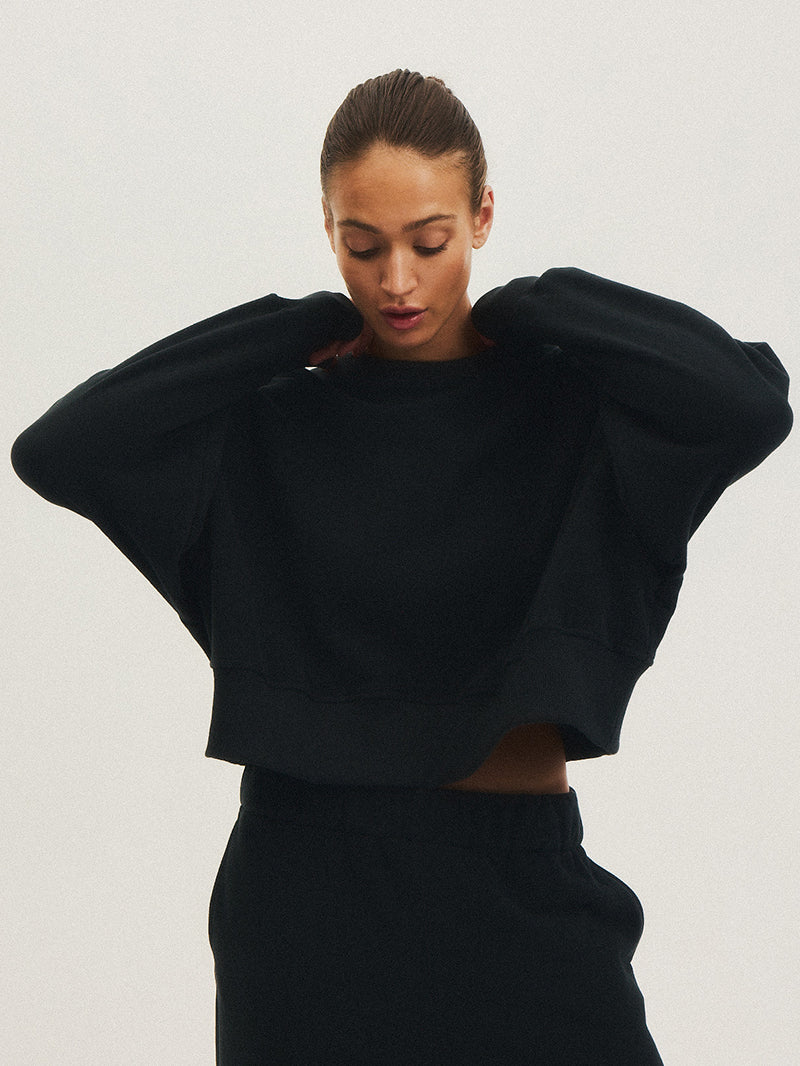 Modelka w czarnej bluzie WAVE JOYINME, unosząca ręce w geście swobody i komfortu